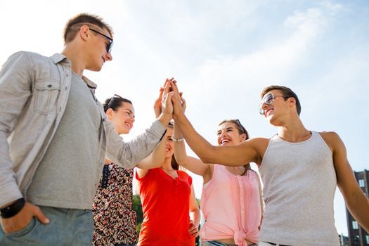 friendship, leisure, summer, gesturer and people concept - group of smiling friends making high five outdoors