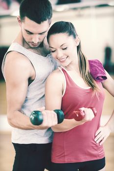 fitness, sport, training, gym and lifestyle concept - two smiling people working out with dumbbells in the gym