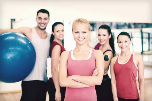 fitness, sport, training, gym and lifestyle concept - smiling woman standing in front of the group of people in gym