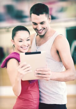 fitness, sport, training, gym and lifestyle concept - two smiling people with tablet pc in the gym