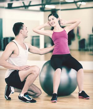 fitness, sport, training, gym and lifestyle concept - male trainer with woman doing crunches on the ball