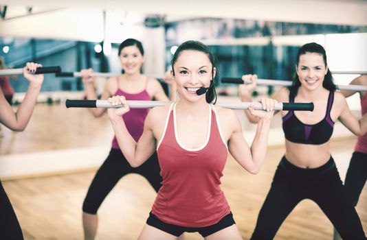 fitness, sport, training, gym and lifestyle concept - smiling trainer in front of the group of people working out with barbells in the gym