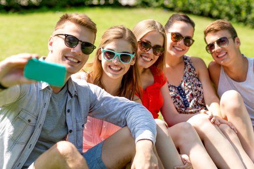 friendship, leisure, summer, technology and people concept - group of smiling friends with smartphone making selfie in park