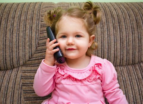 portrait of a cute little girl on chair talking on the phone and watch on viewer
