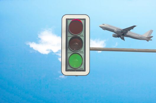 Green color on the traffic light with a beautiful blue sky. In the background, flying a plane.
