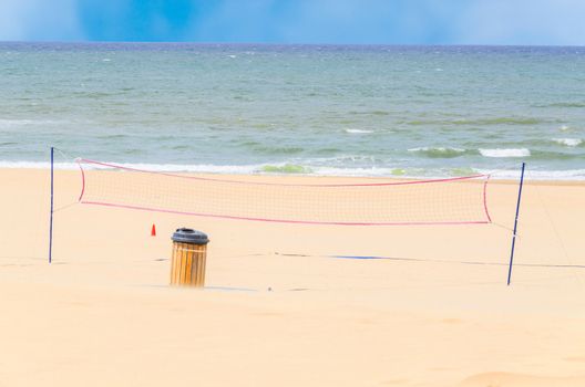 Deserted beach in the foreground, a volleyball net, the blue sea and sky.