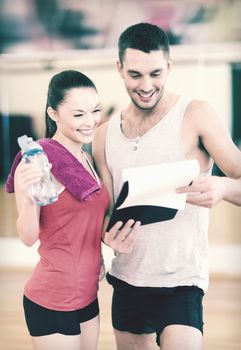 fitness, sport, training, gym and lifestyle concept - smiling male trainer with clipboard and woman with water bottle in the gym