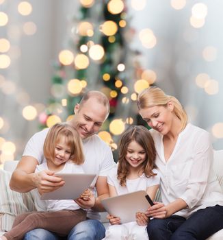 family, holidays, technology and people - smiling mother, father and little girls with tablet pc computers over christmas tree lights background