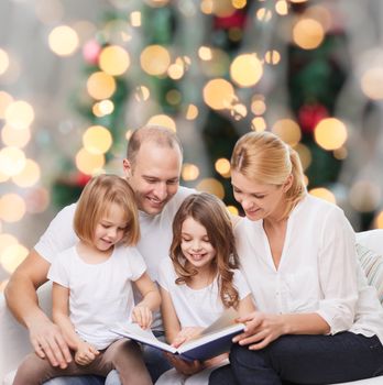 family, childhood, holidays and people - smiling mother, father and little girls reading book over living room and christmas tree background