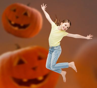 holidays, childhood, happiness and people concept - smiling little girl jumping over halloween pumpkins background