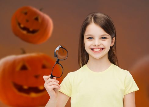 education, holidays, childhood, vision and people concept - smiling little girl in glasses over halloween pumpkins background