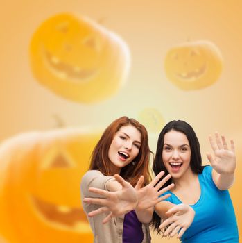 happiness, holidays, friendship and people concept - smiling teenage girls having fun over halloween pumpkins background