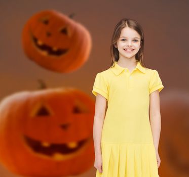 holidays, childhood, happiness and people concept - smiling little girl in dress over halloween pumpkins background