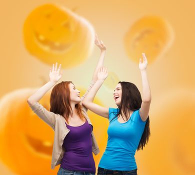 happiness, holidays, friendship and people concept - smiling teenage girls having fun over halloween pumpkins background