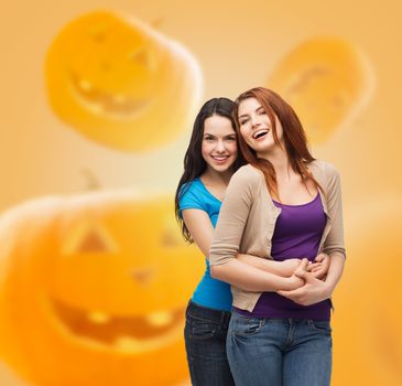 happiness, holidays, friendship and people concept - smiling teenage girls hugging over halloween pumpkins background