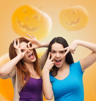 happiness, holidays, friendship and people concept - smiling teenage girls having fun over halloween pumpkins background