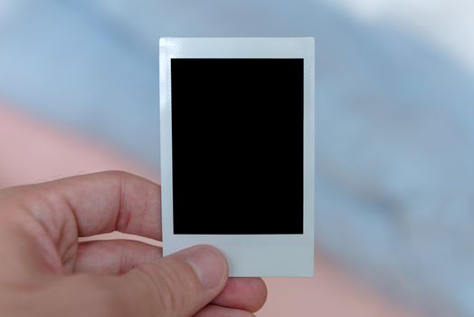 A man's hand holding an instant film print filled with a solid black space to customize with your own picture.