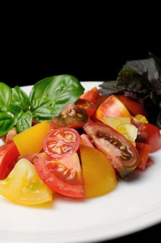 slices of different varieties of tomato with basil on a plate