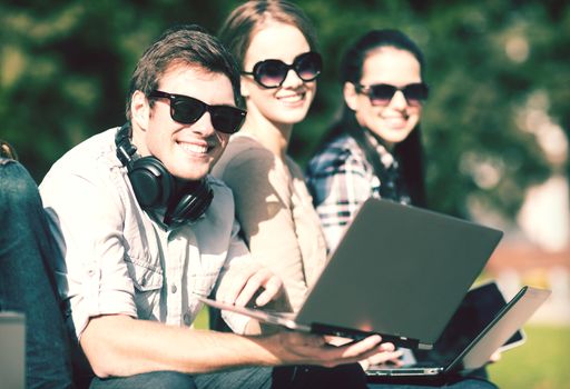 summer, internet, education, campus and teenage concept - group of students or teenagers with laptop and tablet computers hanging out