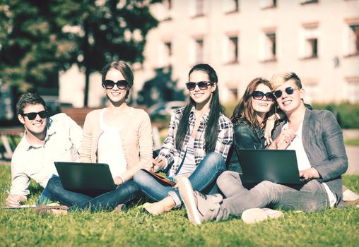 summer, internet, education, campus and teenage concept - group of students or teenagers with laptop, notebooks, files and folders