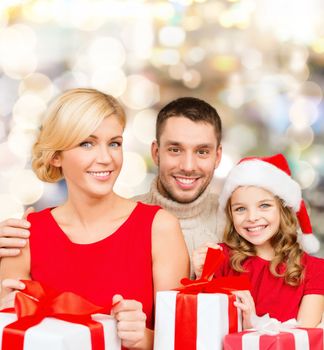 christmas, holidays, family and people concept - happy mother, father and little girl in santa helper hat with gift boxes over lights background