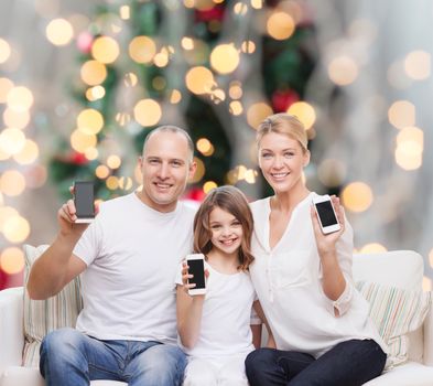 holidays, technology, advertisement and people concept - smiling family with smartphones over living room and christmas tree background