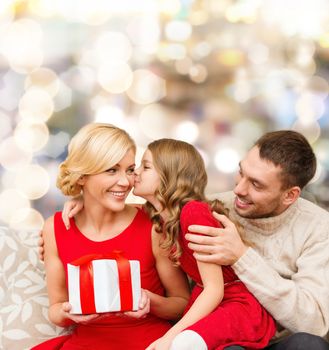 christmas, holidays, family and people concept - happy mother, father and little girl with gift box kissing over lights background