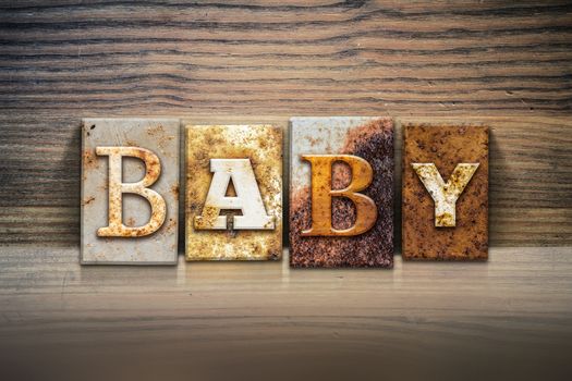 The word "BABY" written in rusty metal letterpress type sitting on a wooden ledge background.