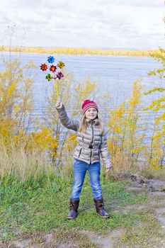 Girl with wind colorful toy on river background in autumn