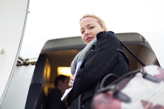 Casually dressed young stylish female traveller boarding airplane in cold winter weather wearing winter coat and wool scarf. Woman on Business travel.