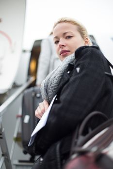 Casually dressed young stylish female traveller boarding airplane in cold winter weather wearing winter coat and wool scarf. Woman on Business travel.