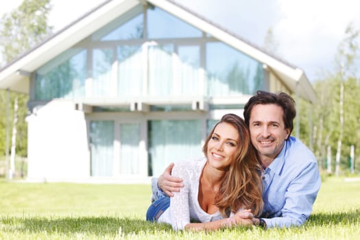 happy couple lying in front of their house