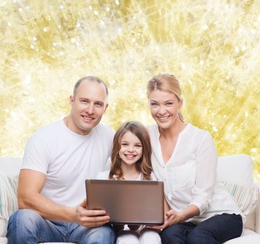 family, childhood, holidays, technology and people concept - smiling family with laptop computer over golden lights background