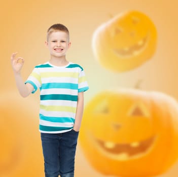 holidays, childhood, happiness, gesture and people concept - smiling little boy showing ok sign over halloween pumpkins background