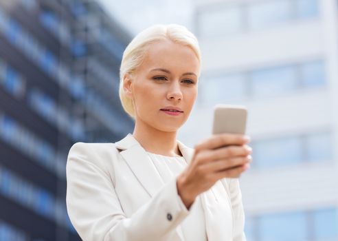 business, technology and people concept - serious businesswoman with smartphone over office building