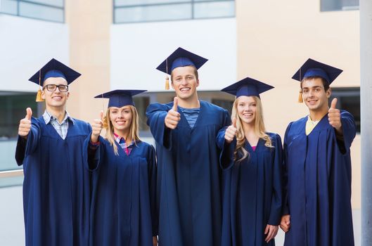 education, graduation, gesture and people concept - group of smiling students in mortarboards and gowns showing thumbs up outdoors