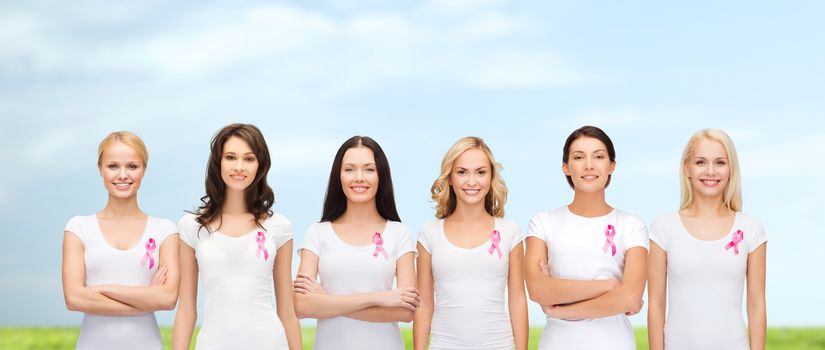 healthcare, people and medicine concept - group of smiling women in blank t-shirts with pink breast cancer awareness ribbons blue sky and grass background