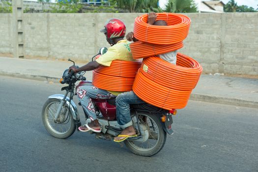 Cotonou, Benin: May 26: A man and a motorcycle taxi operator ride carrying several rolls of garden hose on May 26, 2015 in Cotonou, Benin.