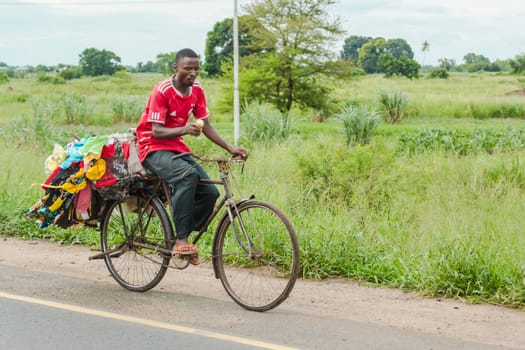 Dar Es Salaam: April 22: A street vendor rides his bike eating his corn on one hand, and carrying his merchandise in the back, on April 22, 2015 in Dar Es Salaam, Tanzania