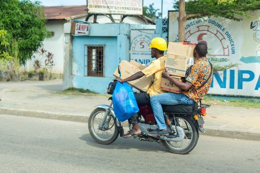 Cotonou, Benin: May 26: A man rides a hired Motorcycle taxi carrying several boxes, the most common means of hired transportation in the city, on May 26, 2015 in Cotonou, Benin.