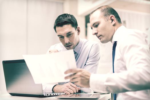 business, technology and office concept - two businessmen with laptop, tablet pc computer and papers having discussion in office