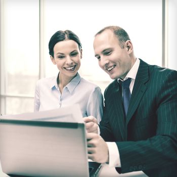 business, technology and office concept - businessman and businesswoman with laptop computer and papers having discussion in office