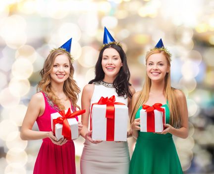 presents, holidays, people and celebration concept - smiling women in party caps with gift boxes over lights background