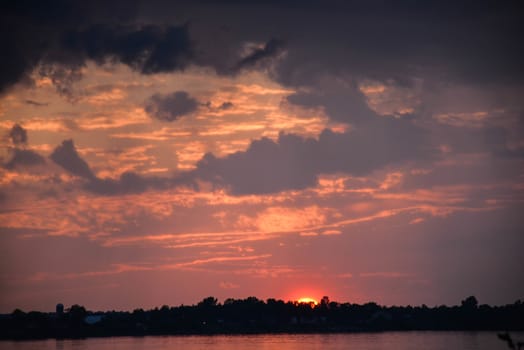 Sun sets through a dramatic sky over a northern lake