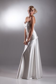 Young beautiful blonde woman in a wedding dress on a studio background