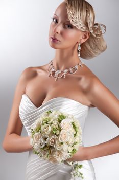 Young beautiful blonde woman in a wedding dress on a studio background