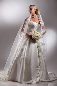 Young beautiful blonde woman in a wedding dress on a studio background