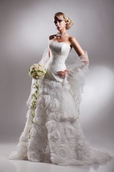 Young beautiful blonde woman in a wedding dress on a studio background