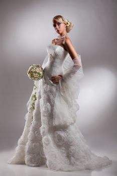 Young beautiful blonde woman in a wedding dress on a studio background