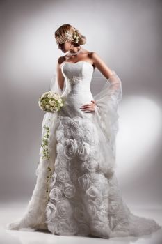 Young beautiful blonde woman in a wedding dress on a studio background